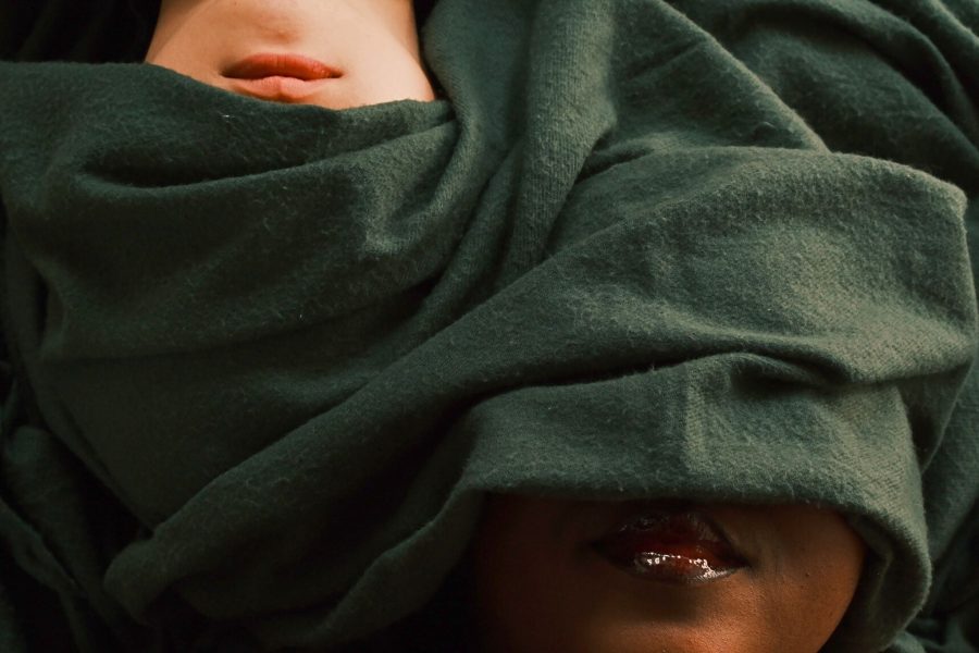 Two faces partially covered by a green cloth, with one face being white and the other black. Only their lips are visible, and the cloth obscures their eyes